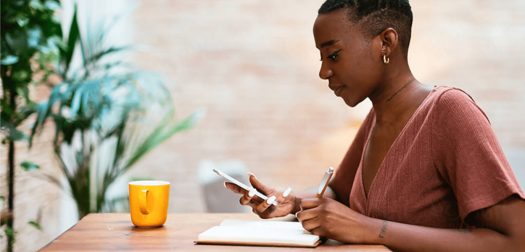 Woman looking at phone while writing in notebook