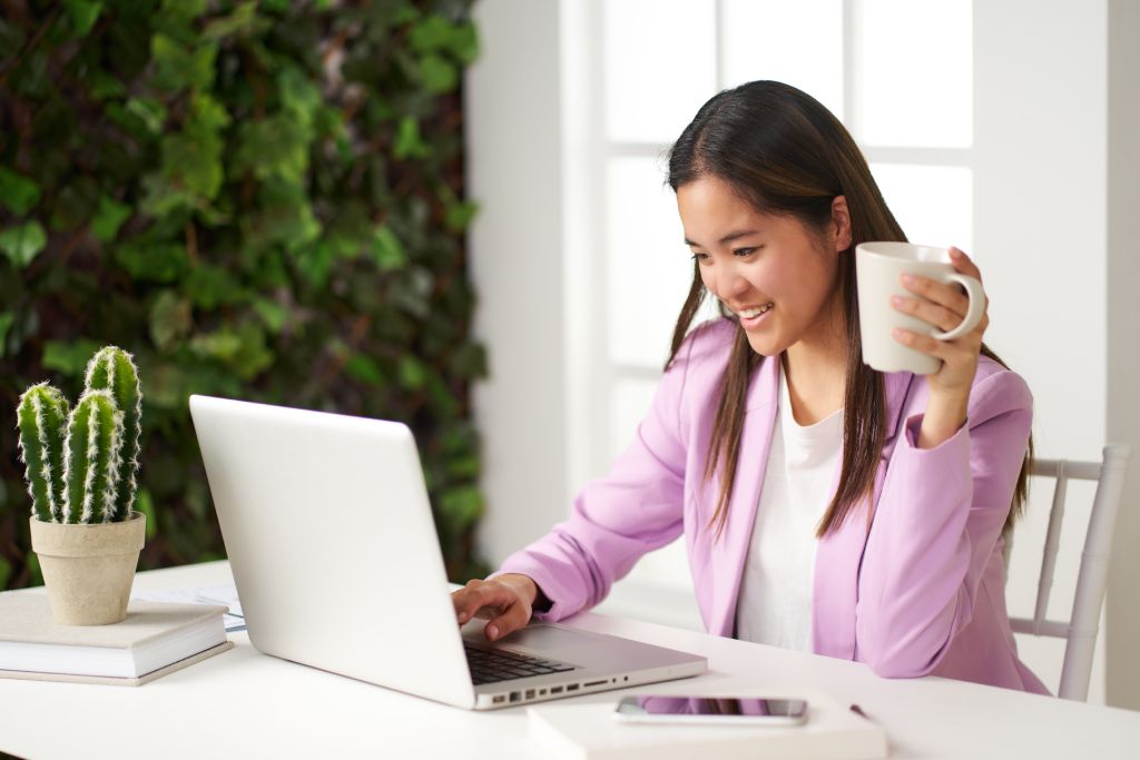 A young remote employee enjoys coffee while attending a virtual staff meeting